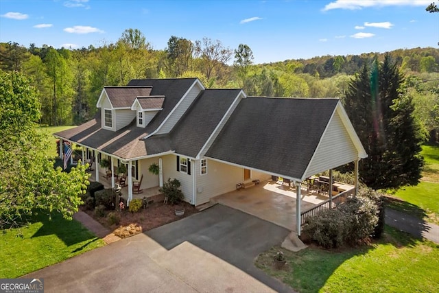 view of front facade featuring a porch, driveway, a carport, and a wooded view