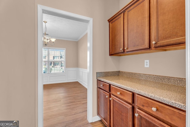 362 Interlake Pass, Mcdonough, GA 30252 - kitchen with ornamental molding, brown cabinetry, light wood-type flooring, a wainscoted wall, and a chandelier