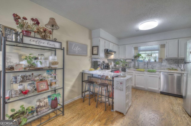 kitchen featuring dishwasher, decorative backsplash, a textured ceiling, and light wood-style flooring