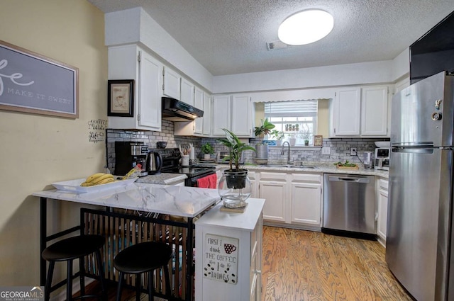 kitchen with stainless steel appliances, a peninsula, a sink, light wood-style floors, and under cabinet range hood