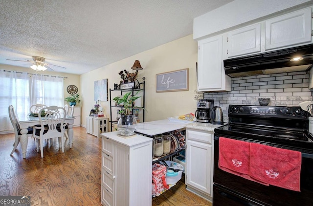 kitchen featuring white cabinets, under cabinet range hood, light countertops, a peninsula, and black range with electric cooktop