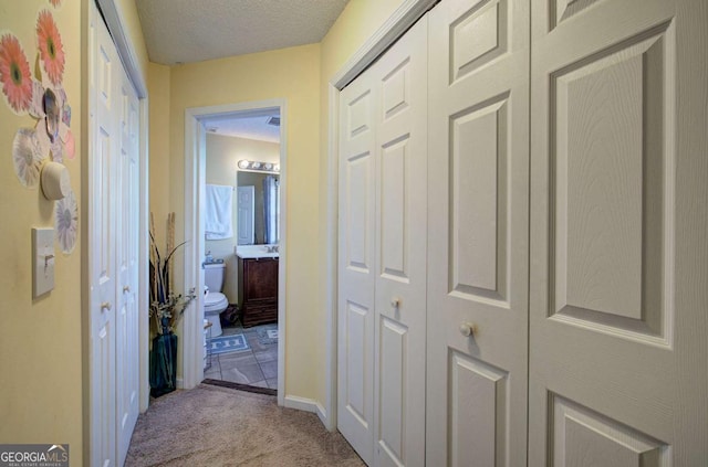 hall featuring baseboards, carpet floors, and a textured ceiling
