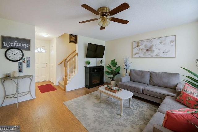 living area with stairway, ceiling fan, a glass covered fireplace, and wood finished floors