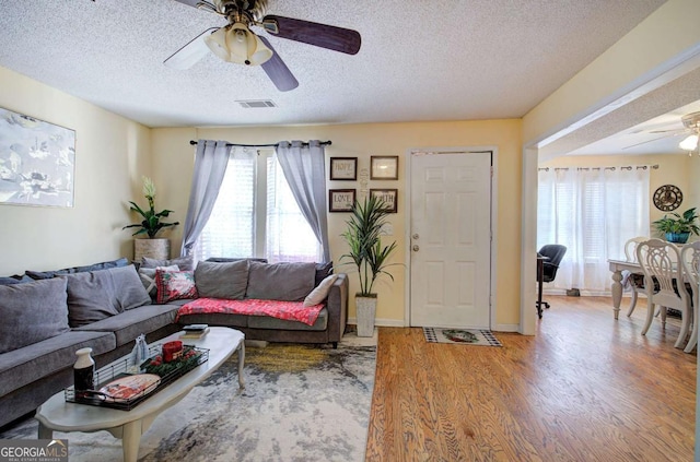 living room with a textured ceiling, baseboards, visible vents, a ceiling fan, and wood finished floors