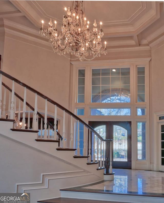 entrance foyer with ornamental molding, a high ceiling, a notable chandelier, and stairs