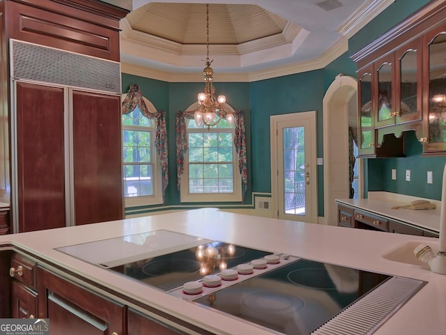 kitchen with light countertops, pendant lighting, black electric stovetop, paneled built in refrigerator, and glass insert cabinets
