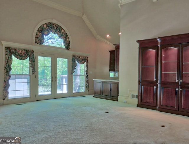unfurnished living room with visible vents, french doors, carpet floors, crown molding, and high vaulted ceiling