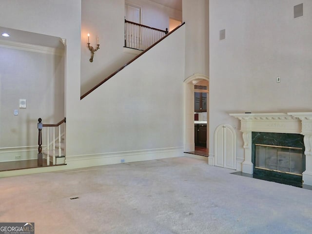 unfurnished living room featuring arched walkways, stairway, carpet flooring, and a towering ceiling