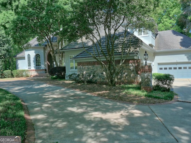 obstructed view of property with an attached garage, concrete driveway, a tiled roof, and stucco siding