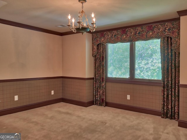 empty room with wainscoting, carpet flooring, a chandelier, and crown molding