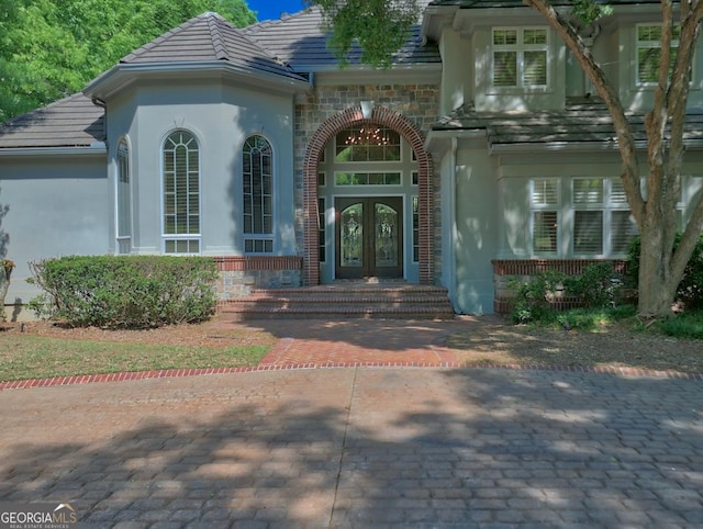doorway to property with stucco siding, a tile roof, stone siding, and french doors