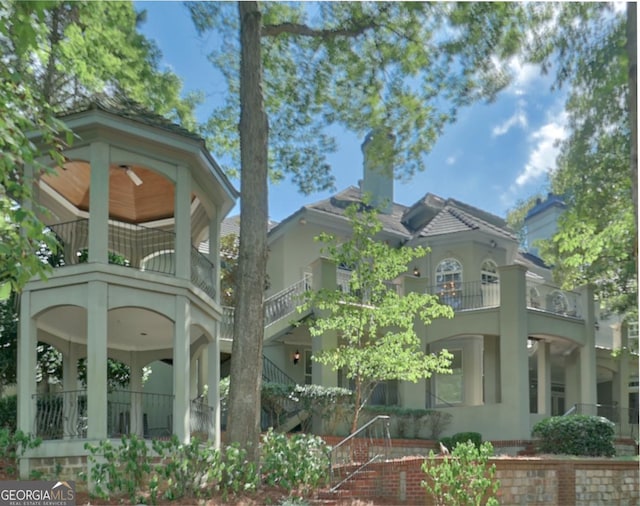 view of side of property featuring stairway, a chimney, a balcony, and stucco siding