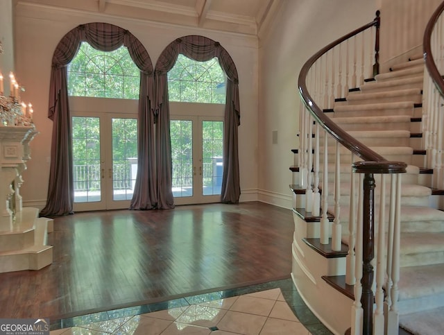 foyer with a towering ceiling, wood finished floors, ornamental molding, french doors, and stairs