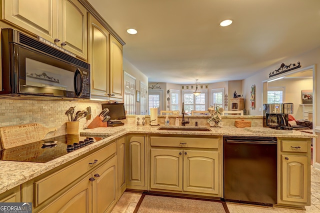 kitchen with light stone countertops, a sink, decorative backsplash, black appliances, and a peninsula
