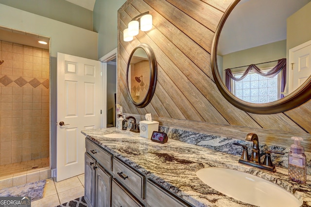 full bath featuring a tile shower, tile patterned flooring, double vanity, and a sink