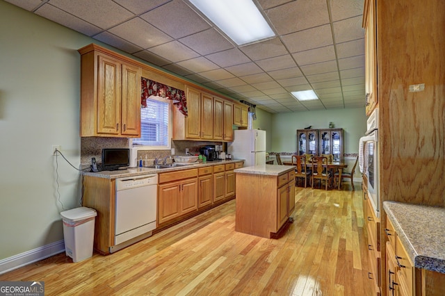 kitchen featuring white appliances, a drop ceiling, a kitchen island, light wood finished floors, and a sink