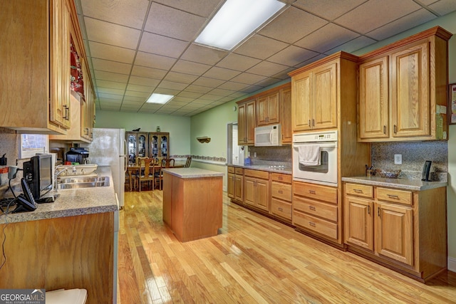 kitchen with white appliances, a kitchen island, backsplash, light wood finished floors, and a sink