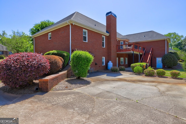 rear view of property with a wooden deck, stairway, brick siding, driveway, and a chimney