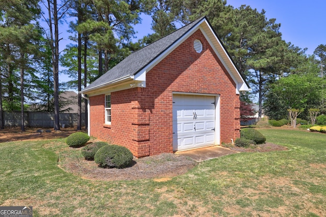 view of home's exterior featuring fence, a detached garage, a shingled roof, a lawn, and brick siding