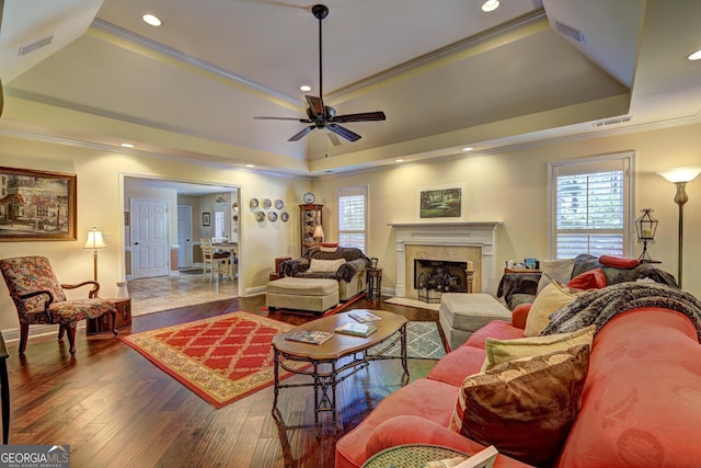 living room with visible vents, a tray ceiling, ornamental molding, a premium fireplace, and a ceiling fan