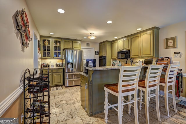 kitchen featuring stainless steel fridge, stone tile flooring, green cabinets, black microwave, and a peninsula