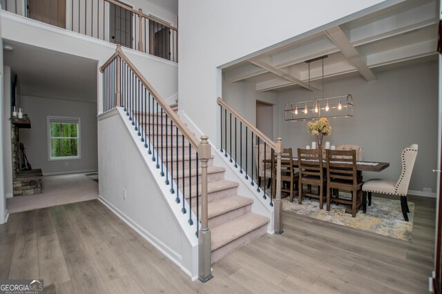 stairs with wood finished floors, coffered ceiling, a chandelier, beamed ceiling, and baseboards