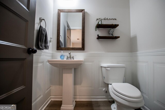 bathroom with a decorative wall, wood finished floors, wainscoting, toilet, and a sink