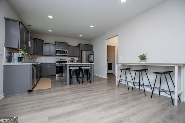 kitchen featuring appliances with stainless steel finishes, a breakfast bar area, recessed lighting, light wood-style floors, and backsplash