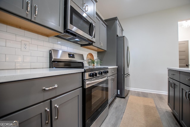 kitchen featuring appliances with stainless steel finishes, backsplash, wood finished floors, and gray cabinets