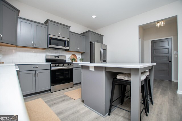 kitchen with appliances with stainless steel finishes, a breakfast bar area, gray cabinets, light countertops, and recessed lighting