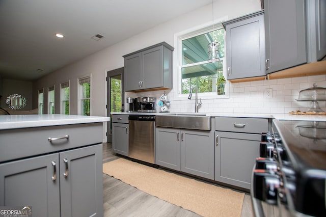 kitchen with gray cabinets, dishwasher, light wood-style flooring, a sink, and tasteful backsplash
