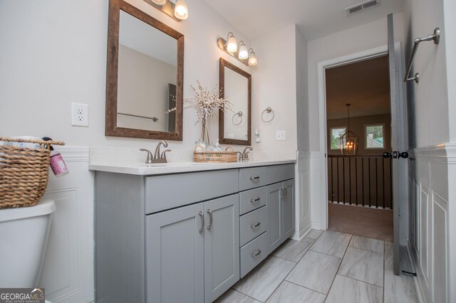 full bathroom with a wainscoted wall, double vanity, toilet, a decorative wall, and marble finish flooring