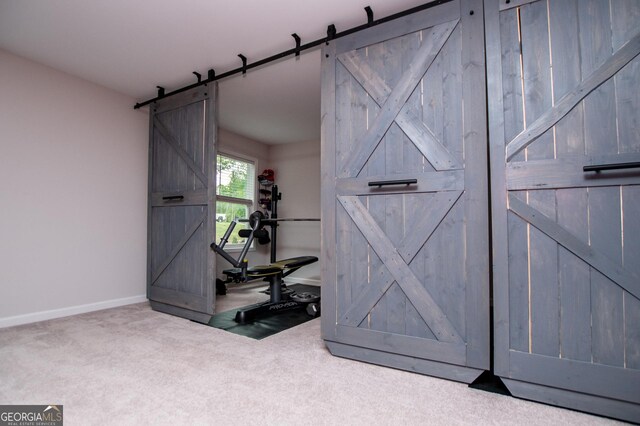 workout room featuring a barn door, carpet floors, and baseboards
