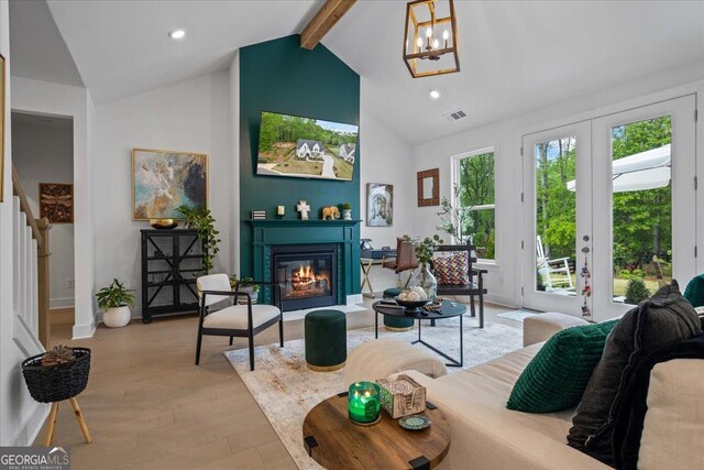 living area featuring an inviting chandelier, visible vents, light wood-type flooring, beam ceiling, and a glass covered fireplace