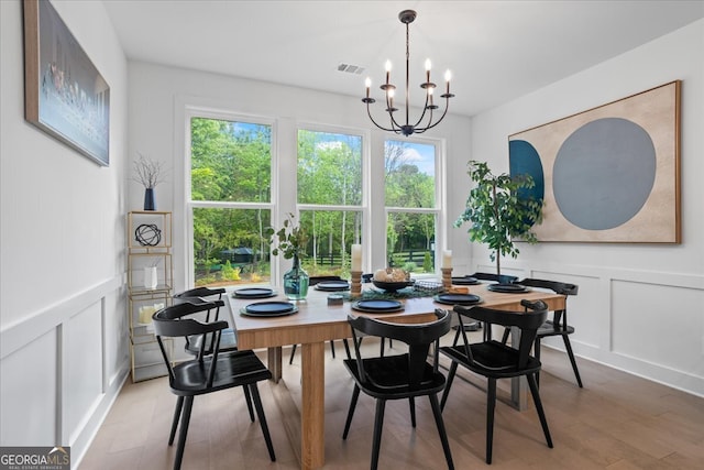 dining room featuring light wood finished floors, a healthy amount of sunlight, a chandelier, and a decorative wall