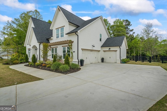 view of home's exterior with an attached garage, roof with shingles, concrete driveway, and fence