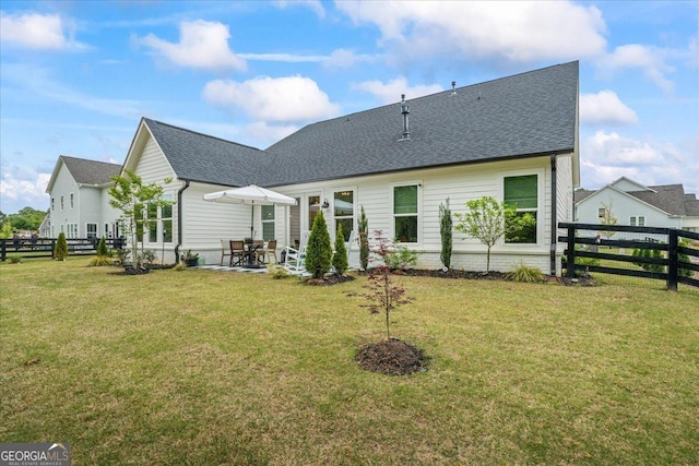 rear view of house with a lawn, a shingled roof, a patio, and fence