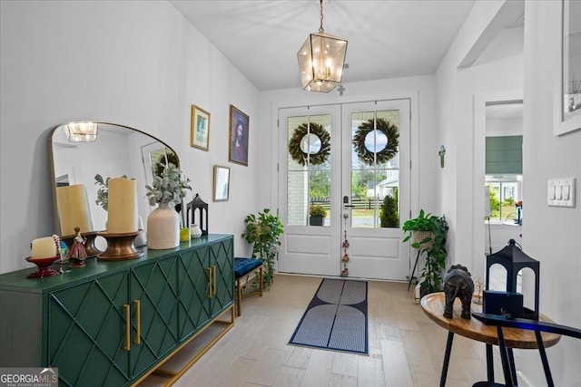 entryway with french doors, an inviting chandelier, and light wood-style flooring
