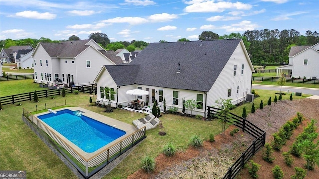 back of property with a lawn, a fenced backyard, cooling unit, a fenced in pool, and roof with shingles