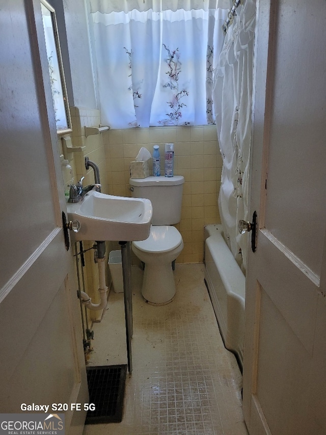 bathroom featuring toilet, tile walls, and a sink