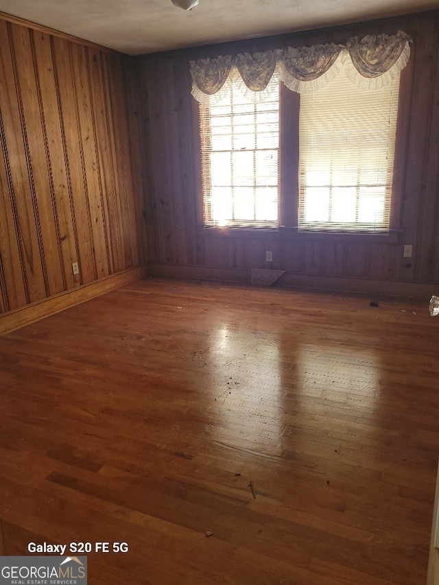 empty room featuring wood finished floors, wooden walls, and a wealth of natural light
