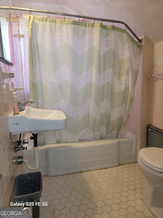 bathroom featuring tile patterned floors, shower / bath combo with shower curtain, toilet, and tile walls