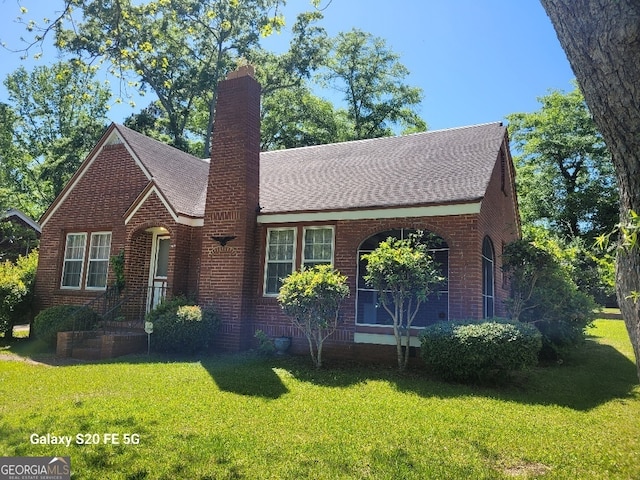 view of front of home featuring brick siding, a shingled roof, a chimney, and a front yard