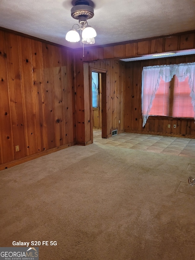 empty room featuring visible vents, carpet floors, a healthy amount of sunlight, wooden walls, and a textured ceiling