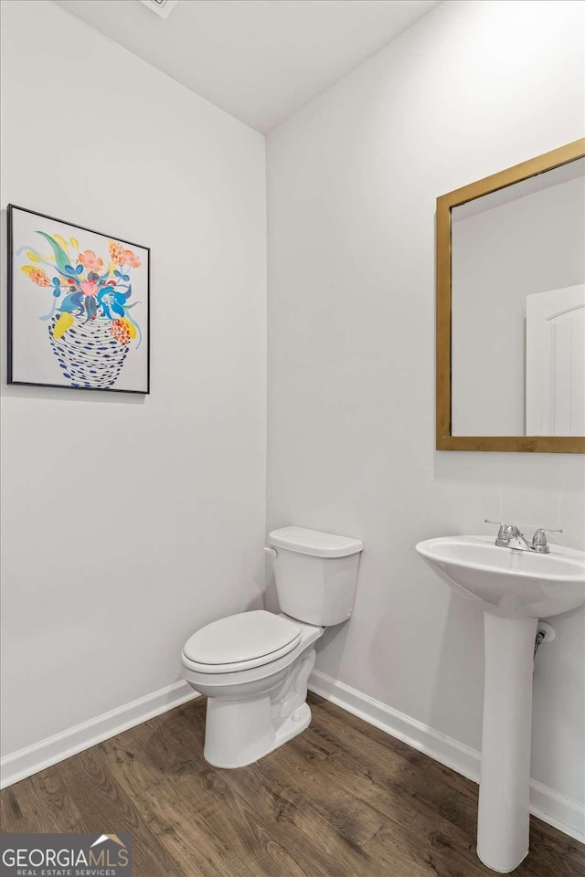 bathroom featuring wood finished floors, baseboards, toilet, and a sink