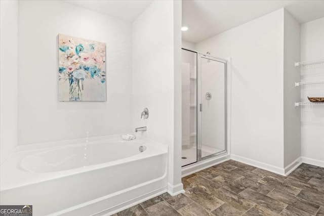 bathroom with a stall shower, a garden tub, and baseboards