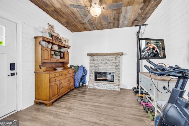 interior space featuring wood ceiling, light wood-style floors, ceiling fan, a fireplace, and wooden walls