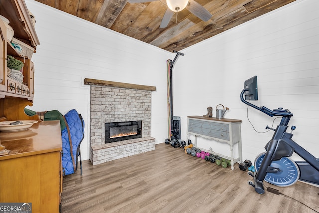 exercise room featuring wooden ceiling, wood finished floors, a ceiling fan, and a fireplace