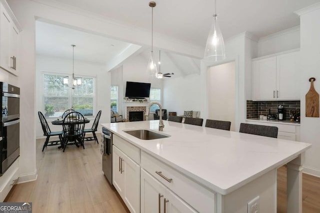 kitchen with a sink, dishwasher, light wood finished floors, white cabinetry, and a brick fireplace