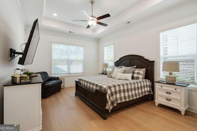 bedroom with a raised ceiling, visible vents, light wood finished floors, and baseboards
